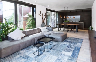 Dostatek přirozeného denního světla a propojení interiéru s exteriérem celý prostor opticky zvětšuje. Efektně působí také kuchyň na míru z černě mořeného dubu pokrývající celou jednu stěnu místnosti, která tvoří harmonický kontrast s převažující bílou výmalbou a pokoj vizuálně prohlubuje