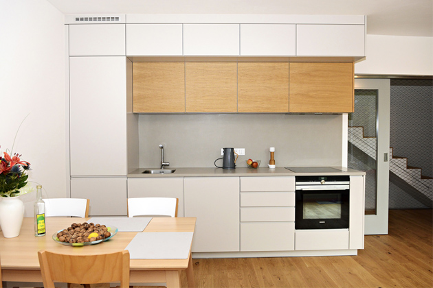Malá kuchyň ve velkém domě v provedení šedý matný lak s frézovaným J profilem v kombinaci s dubovou dýhou na horních skříňkách. Pracovní deska a zástěna jsou z keramiky. Zvýšené spodní skříňky na přání zákazníků