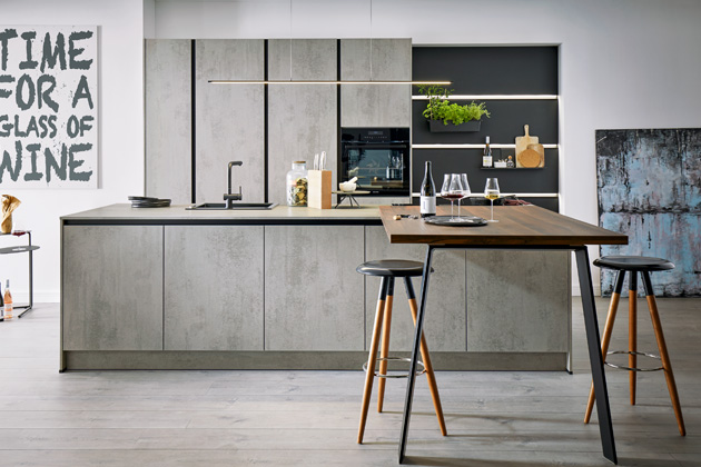 Moderní kuchyně Elba (Schüller) v imitaci betonu s ostrůvkem, který navazuje na jídelní stůl, za čistými liniemi stojí bezúchytkové otevírání, které je řešené na TIP-ON