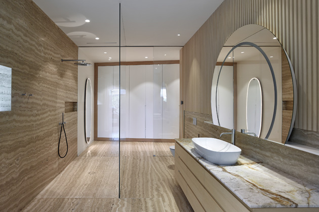 Koupelna u ložnice majitelů je koncipovaná jako tzv. wet room, v němž se sprchový kout prolíná se zbytkem místnosti. Toto řešení umocňuje pocit vzdušnosti a prostoru, zároveň klade vysoké nároky na použité materiály – v tomto případě dominantní Travertino romano, které je v místech s přímým kontaktem s vodou zataženo pryskyřicí. 