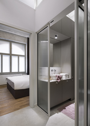 Do ložnice s šatnou a koupelnou se dostanete skrze ukryté dveře, které naprosto splývají s dřevěným obkladem. Je v ní dřevěná parketová podlaha. Architekti hojně užívali zabudovaných LED pásků v nábytku, které mají několik světelných režimů. Takto dokázali vytvořit světlo blížící se dennímu osvětlení i ambientní osvětlení pro večerní čas. Stejný princip je zde použit pro každou místnost. Světlík mezi ložnicí a koupelnou má akustickou úpravu. Čalouněné lůžko se zabudovaným úložným prostorem ve výsuvech je vyrobeno podle návrhu architektů. Nastavitelné svítidlo (Flos) z nerezové oceli, umístěné u postele, je od designéra a architekta Vincenta Van Duysena. 