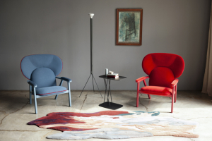 Křeslo Peggy kombinuje čalouněnou skořápku s obepínající opěrkou hlavy, podstavec z jasanového dřeva a jemně tvarované područky pro elegantní pohodlí a vizuální lehkost.