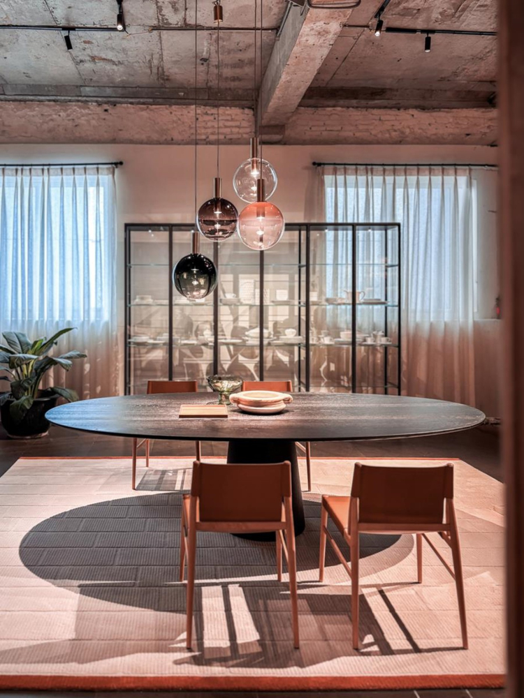 V j&iacute;deln&iacute; z&oacute;ně upout&aacute; pozornost geometrick&yacute; stůl Materic Oval od design&eacute;ra Piera Lissoniho s deskou a podnož&iacute; z černě mořen&eacute;ho jasanu. K němu se poj&iacute; židle Voyage, kter&eacute; navrhl design&eacute;rsk&yacute; tandem GamFratesi 